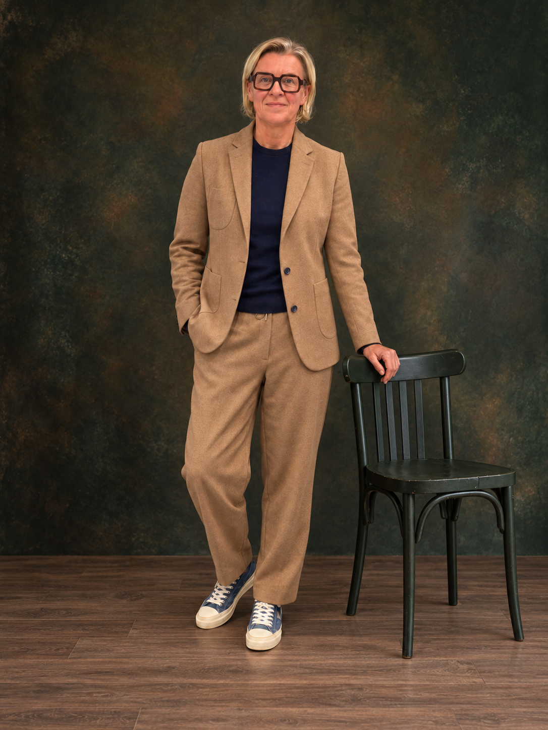 Damenanzug in Camel mit dunkelblauem Strick und blauen Sneakern im Fotostudio